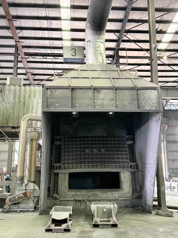 The remelting furnace beneath its fume hood, the charging opening dark